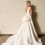 Back view of textured Mikado A-line wedding dress with deep V-back, detachable bow detail, and flowing chapel train.
