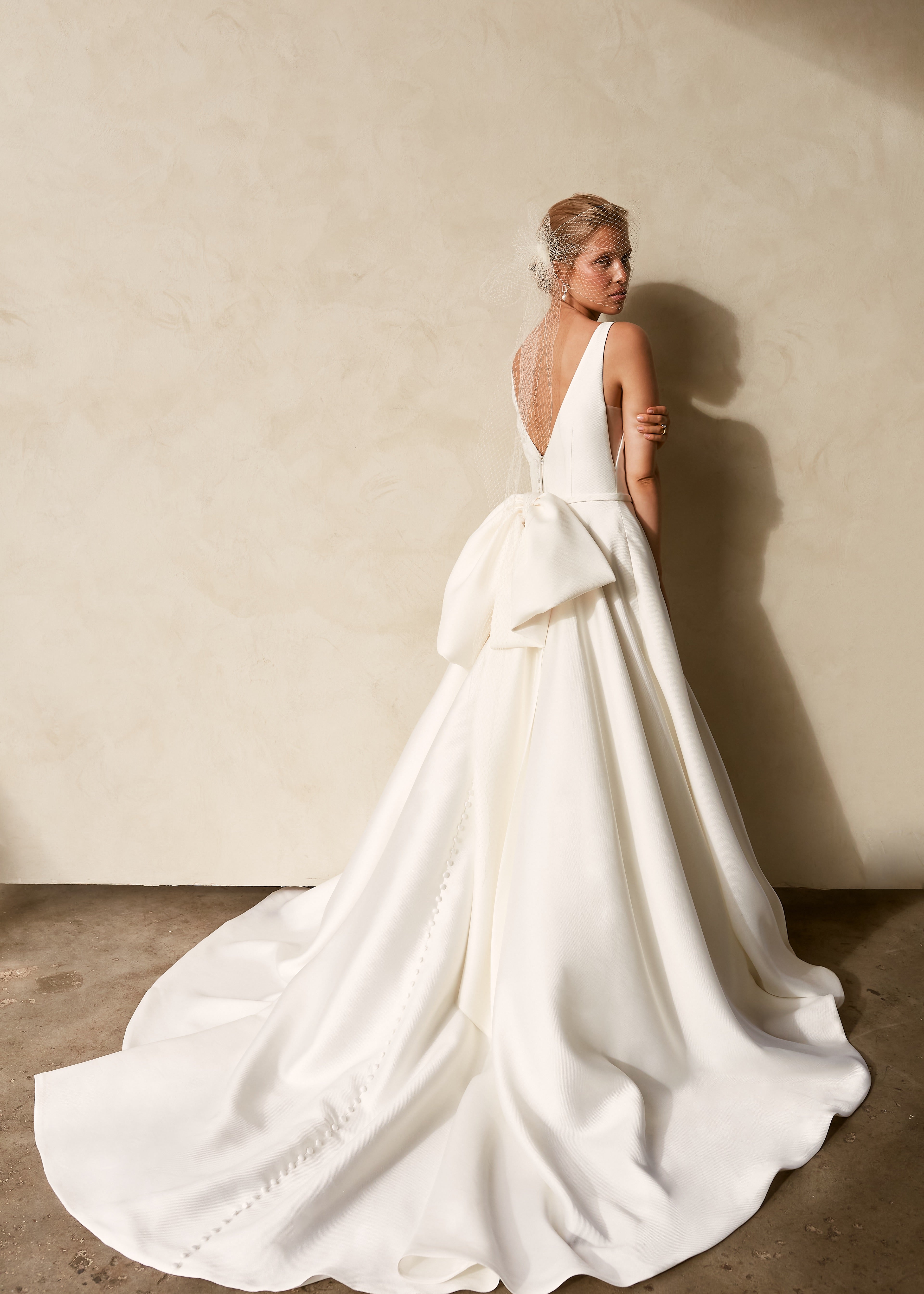 Back view of textured Mikado A-line wedding dress with deep V-back, detachable bow detail, and flowing chapel train.
