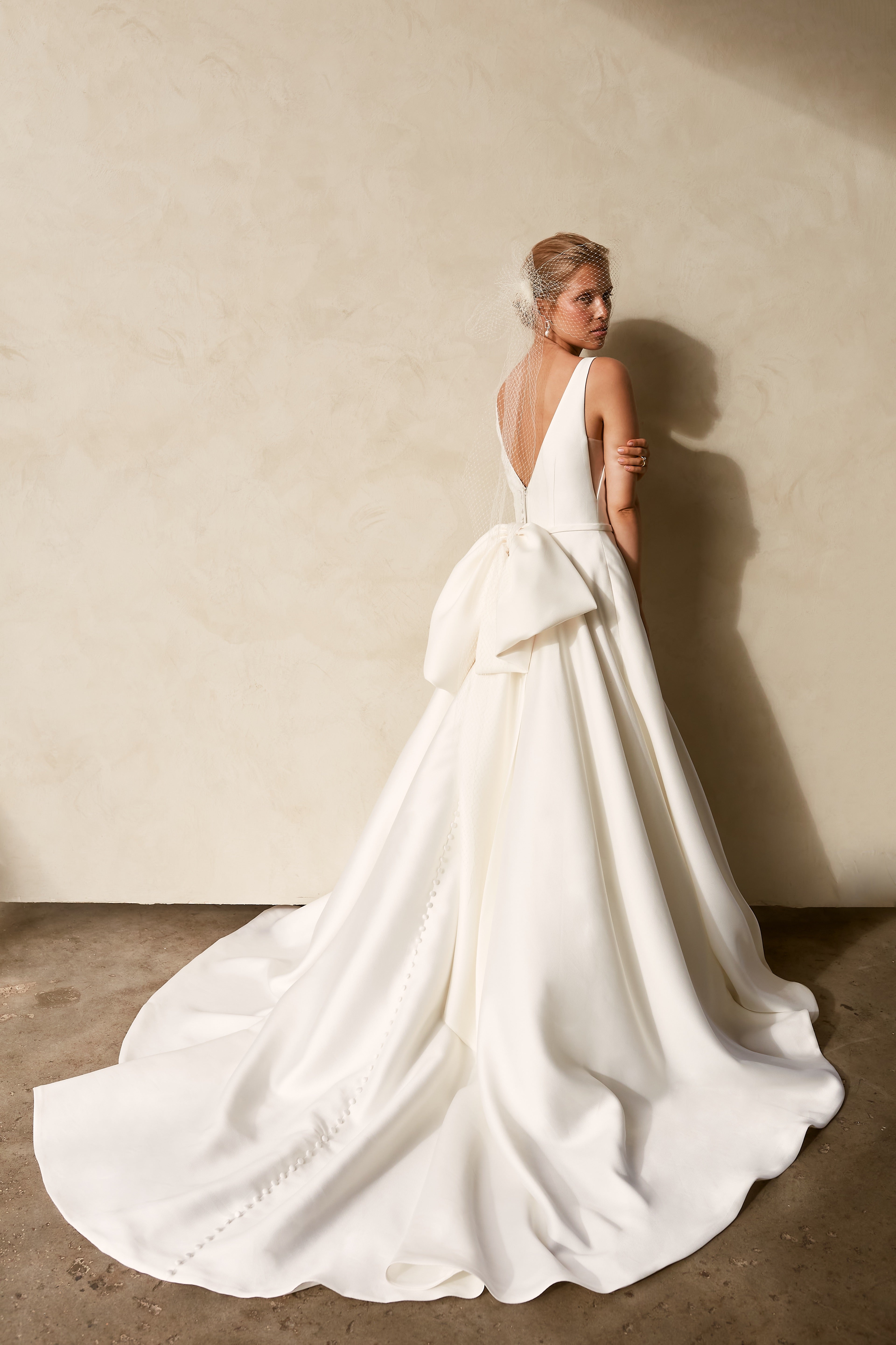 Back view of textured Mikado A-line wedding dress with deep V-back, detachable bow detail, and flowing chapel train.
