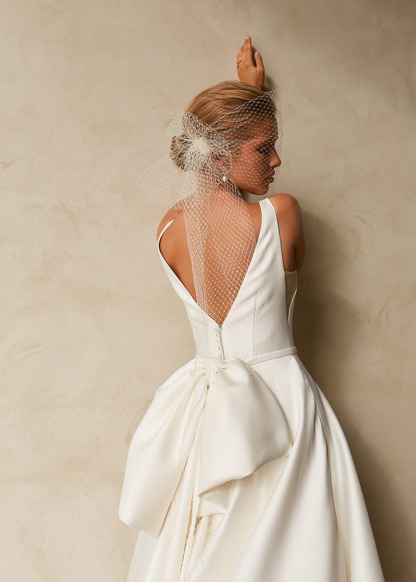 Close-up back view of textured Mikado A-line wedding dress with deep V-back, detachable bow, and bridal birdcage veil.