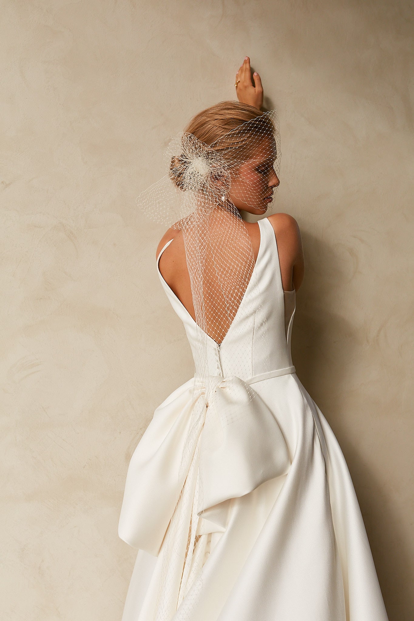 Close-up back view of textured Mikado A-line wedding dress with deep V-back, detachable bow, and bridal birdcage veil.