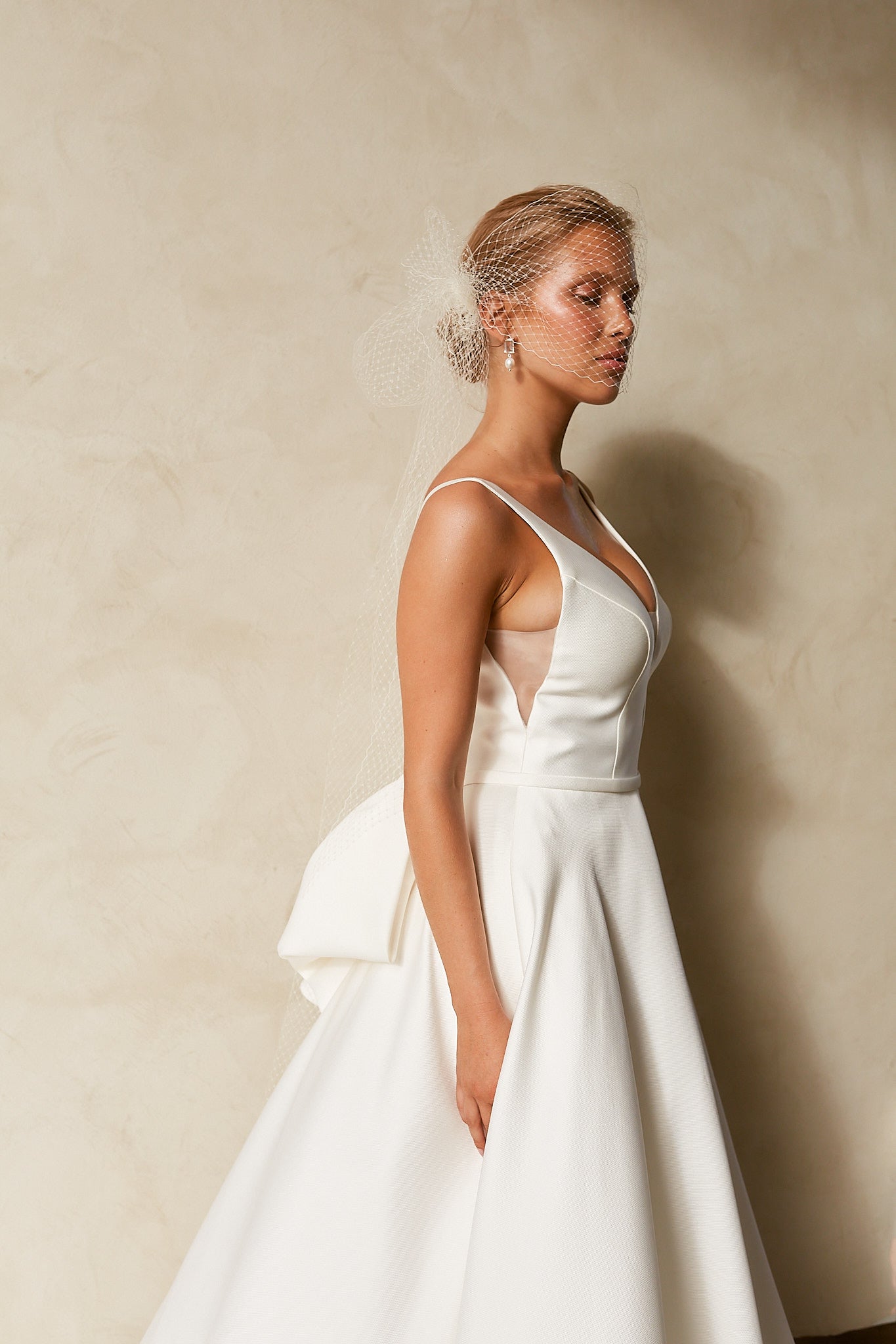 Side view of textured Mikado A-line wedding dress with deep V neckline, structured bodice, and detachable bow detail.
