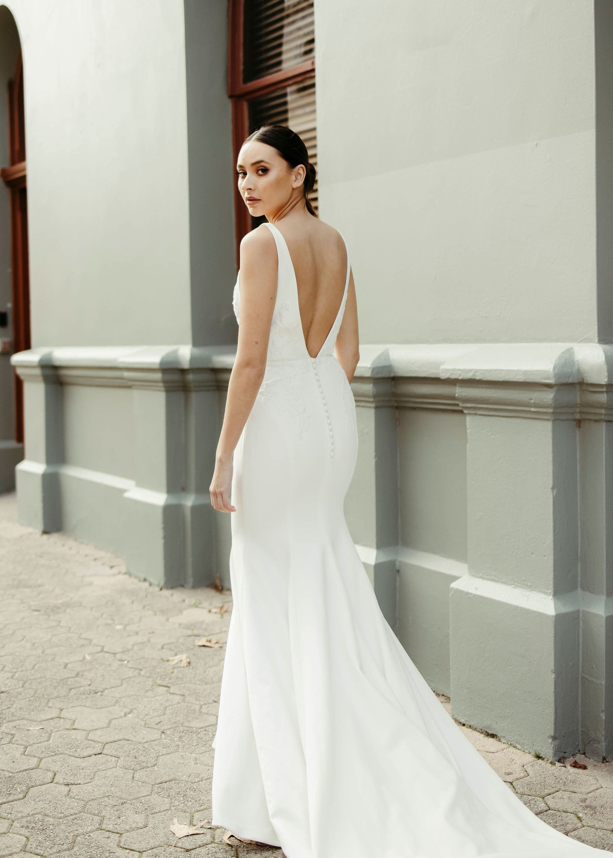 Back view of crepe fit and flare wedding dress with deep V-back, delicate lace bodice detailing, and flowing train.