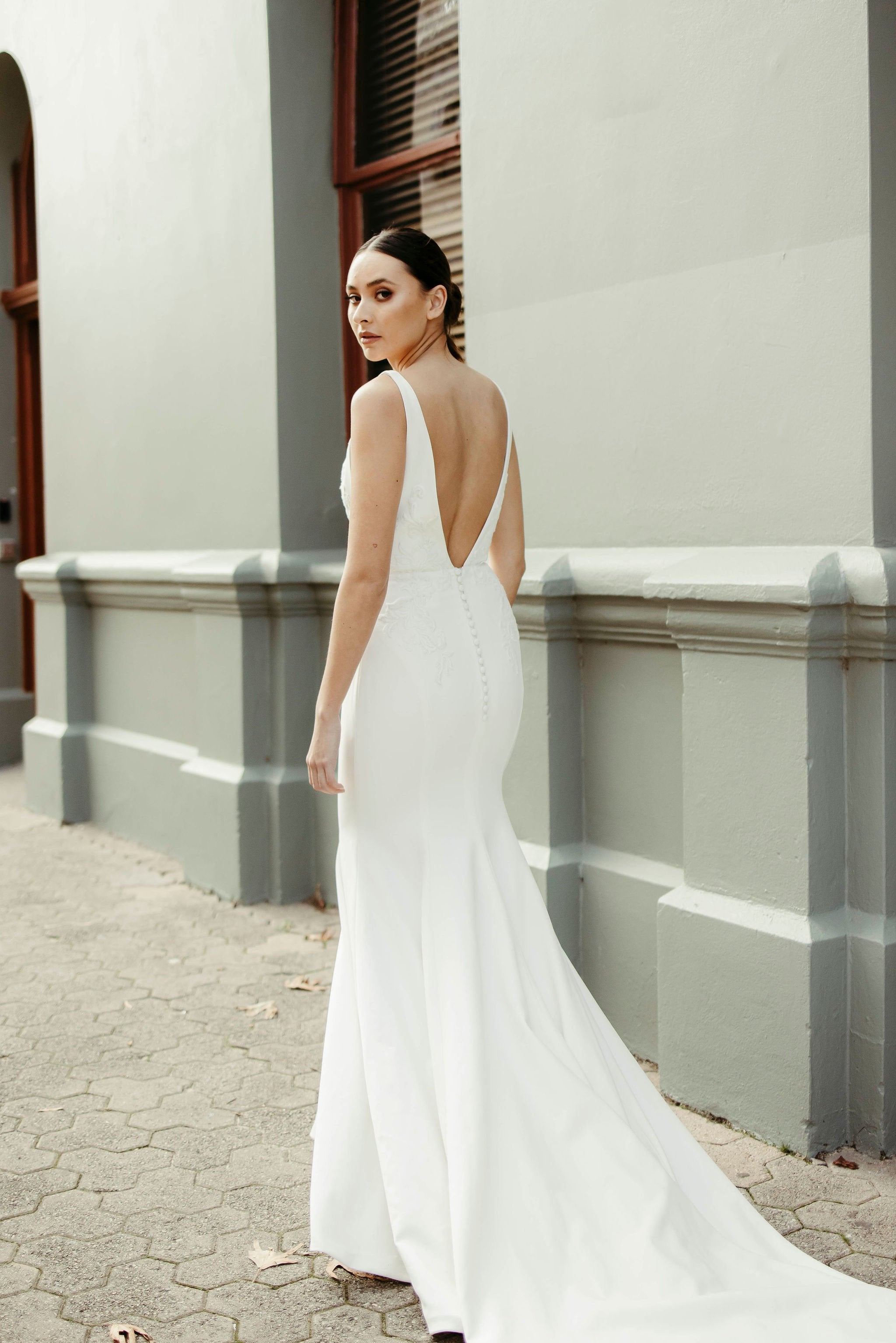 Back view of crepe fit and flare wedding dress with deep V-back, delicate lace bodice detailing, and flowing train.