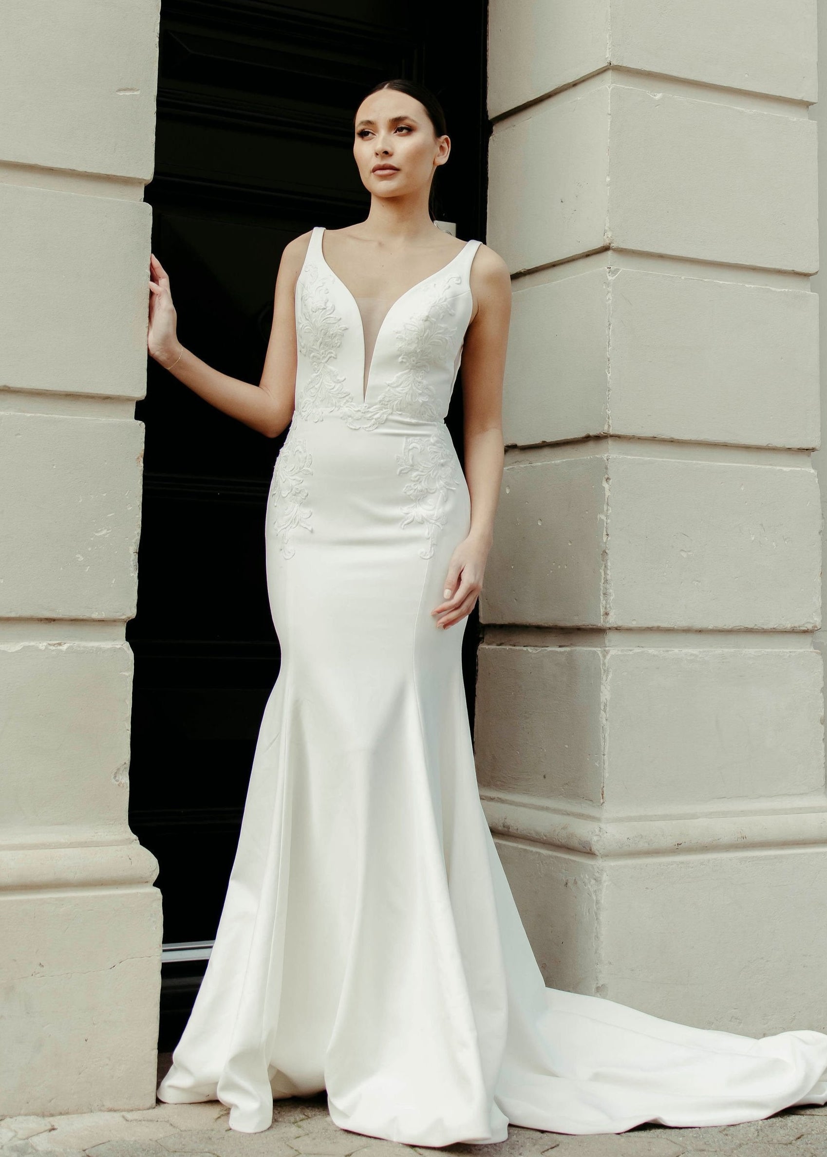 Crepe fit and flare wedding dress with soft V neckline, delicate lace detailing on the bodice, and flowing train.