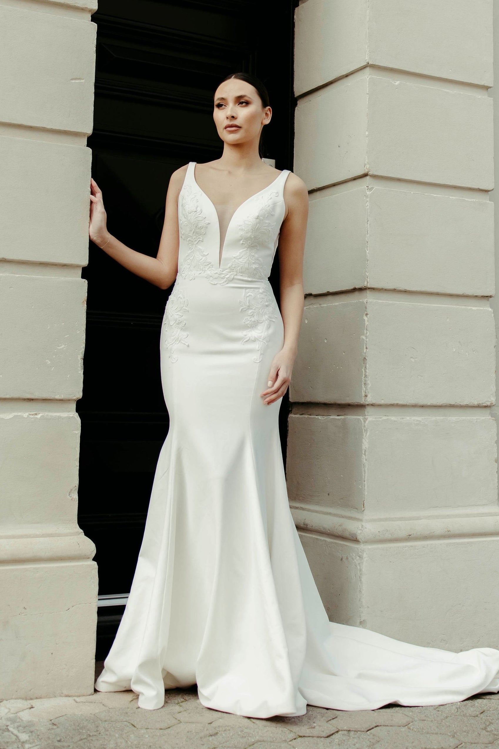 Crepe fit and flare wedding dress with soft V neckline, delicate lace detailing on the bodice, and flowing train.