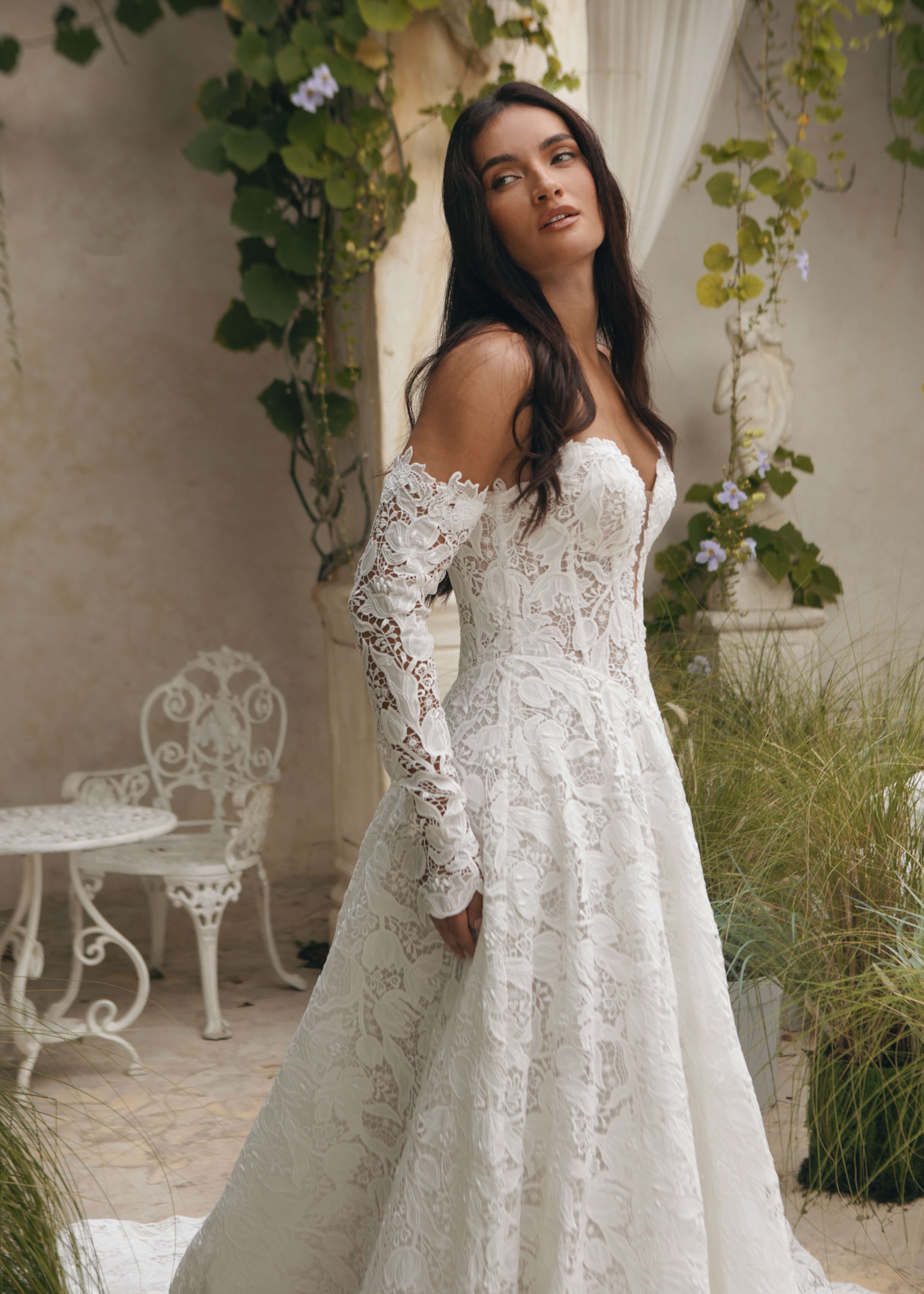 Woman in a white Lace A-Line Wedding Dress standing in an outdoor setting with greenery and a table.