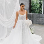 Woman in a A-Line Wedding Dress holding flowers with a white curtain and greenery in the background