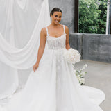 Woman in a A-Line Wedding Dress holding flowers with a white curtain and greenery in the background