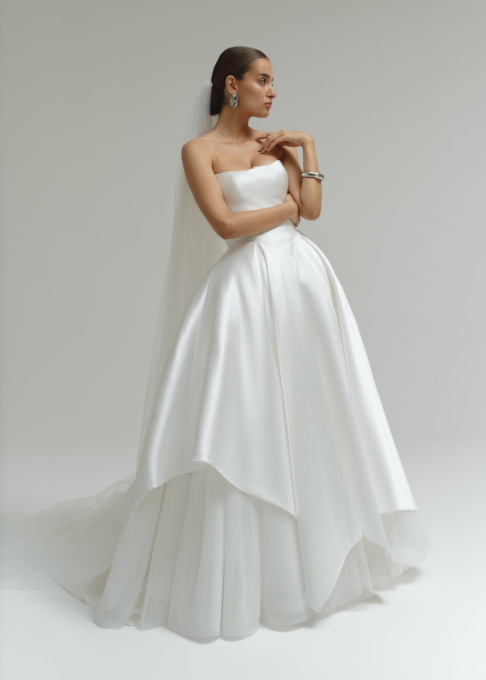 Woman wearing a strapless Mikado ballgown wedding dress  on a plain background