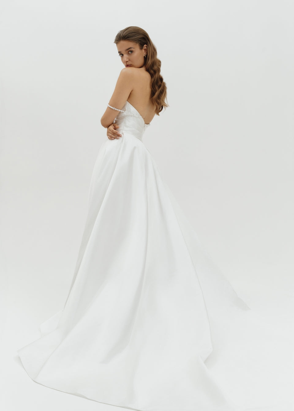 Woman wearing a Duchess satin basque waist wedding dress on a plain background