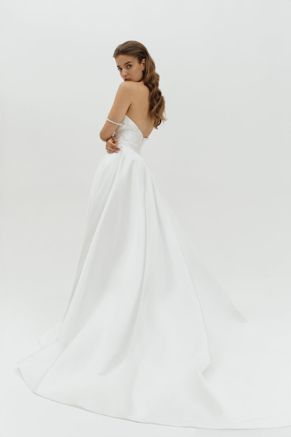 Woman wearing a Duchess satin basque waist wedding dress on a plain background