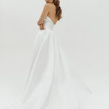 Woman wearing a Duchess satin basque waist wedding dress on a plain background