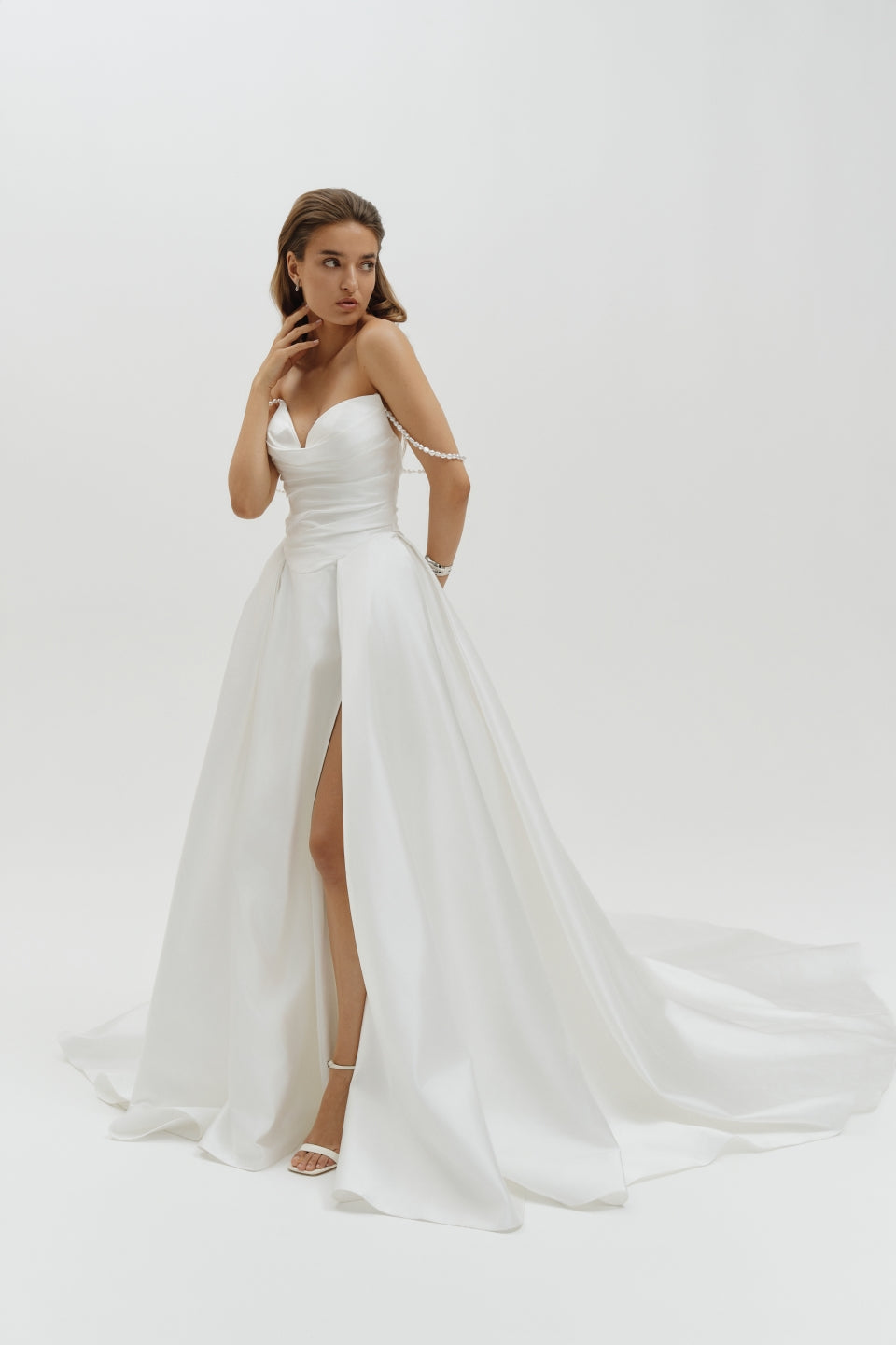 Woman wearing a Duchess satin basque waist wedding dress with a slit on a white background