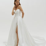 Woman wearing a Duchess satin basque waist wedding dress with a slit on a white background