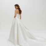 Woman wearing a basque waist Mikado ballgown wedding dress with a long train on a plain background