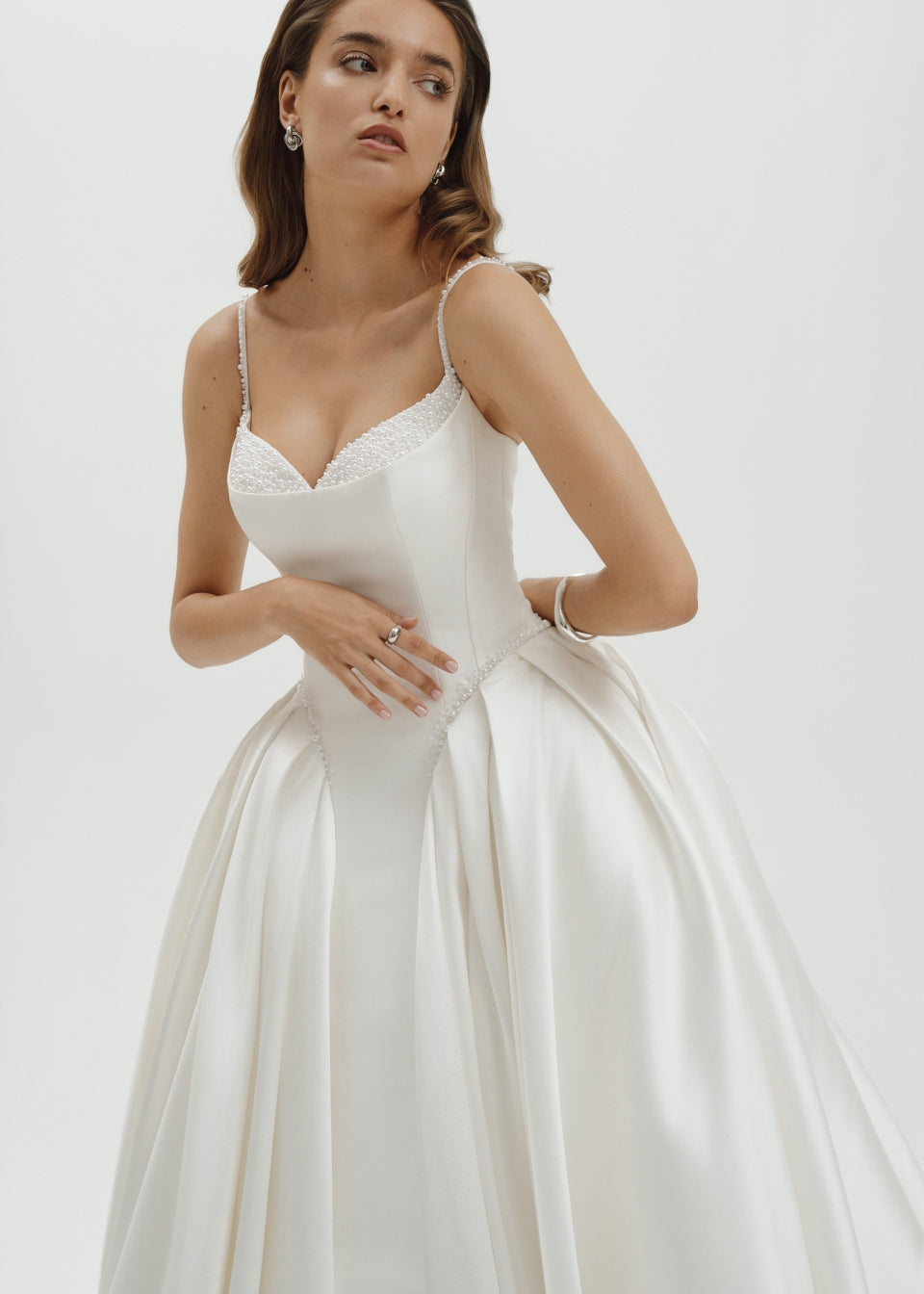 Woman wearing a basque waist Mikado ballgown wedding dress against a plain background
