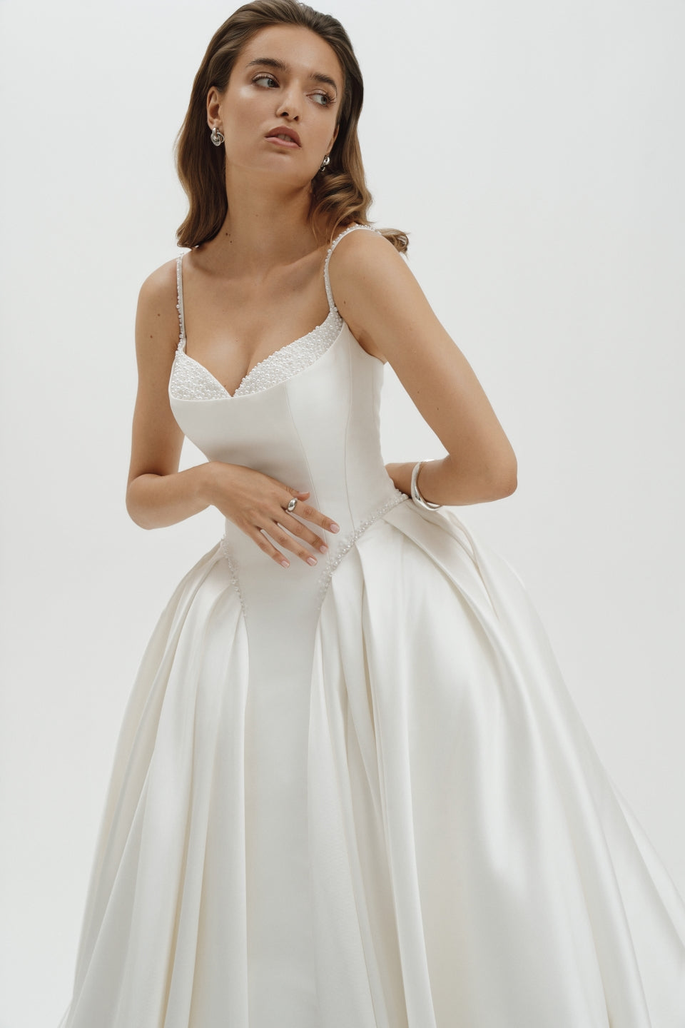 Woman wearing a basque waist Mikado ballgown wedding dress against a plain background