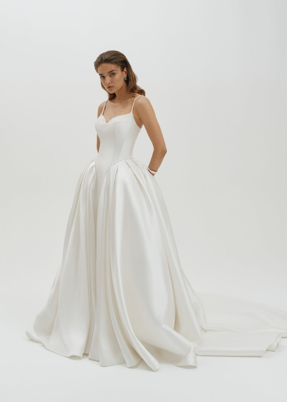 Woman wearing a basque waist Mikado ballgown wedding dress  on a plain background