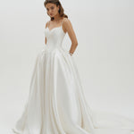 Woman wearing a basque waist Mikado ballgown wedding dress  on a plain background