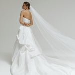Woman in a strapless matte satin bubble wedding dress with a long veil on a plain background
