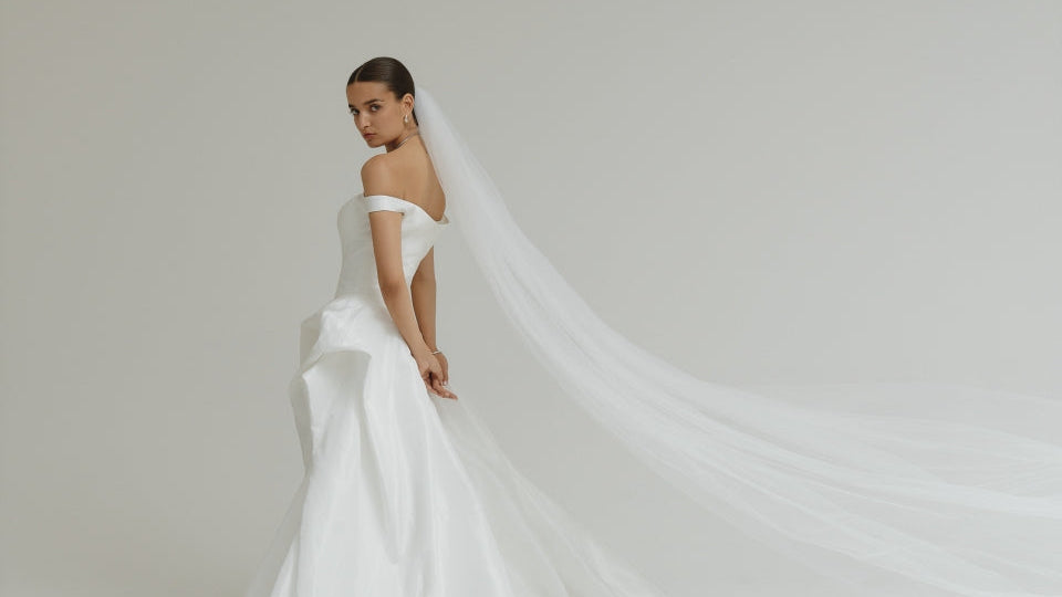 Bride in a white wedding dress with a long veil against a plain background