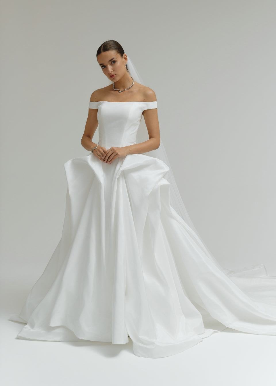 Woman wearing a off-the-shoulder matte satin ballgown wedding dress on a plain background