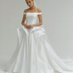 Woman wearing a off-the-shoulder matte satin ballgown wedding dress on a plain background
