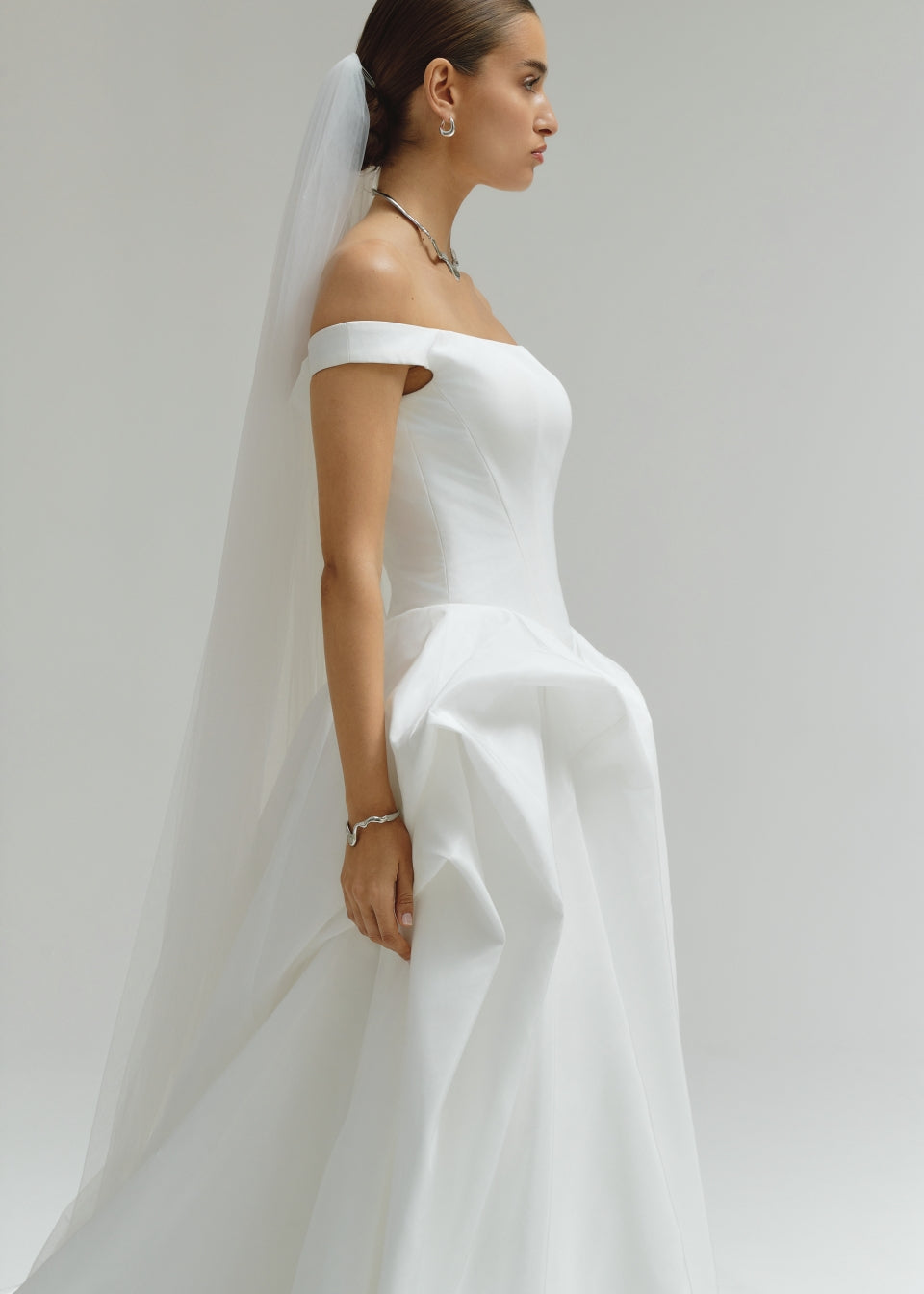 Woman wearing a white wedding dress with a veil against a plain background