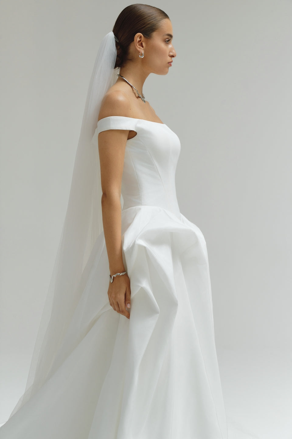 Woman wearing a white wedding dress with a veil against a plain background