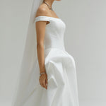 Woman wearing a white wedding dress with a veil against a plain background