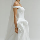 Woman wearing a white wedding dress with a veil against a plain background