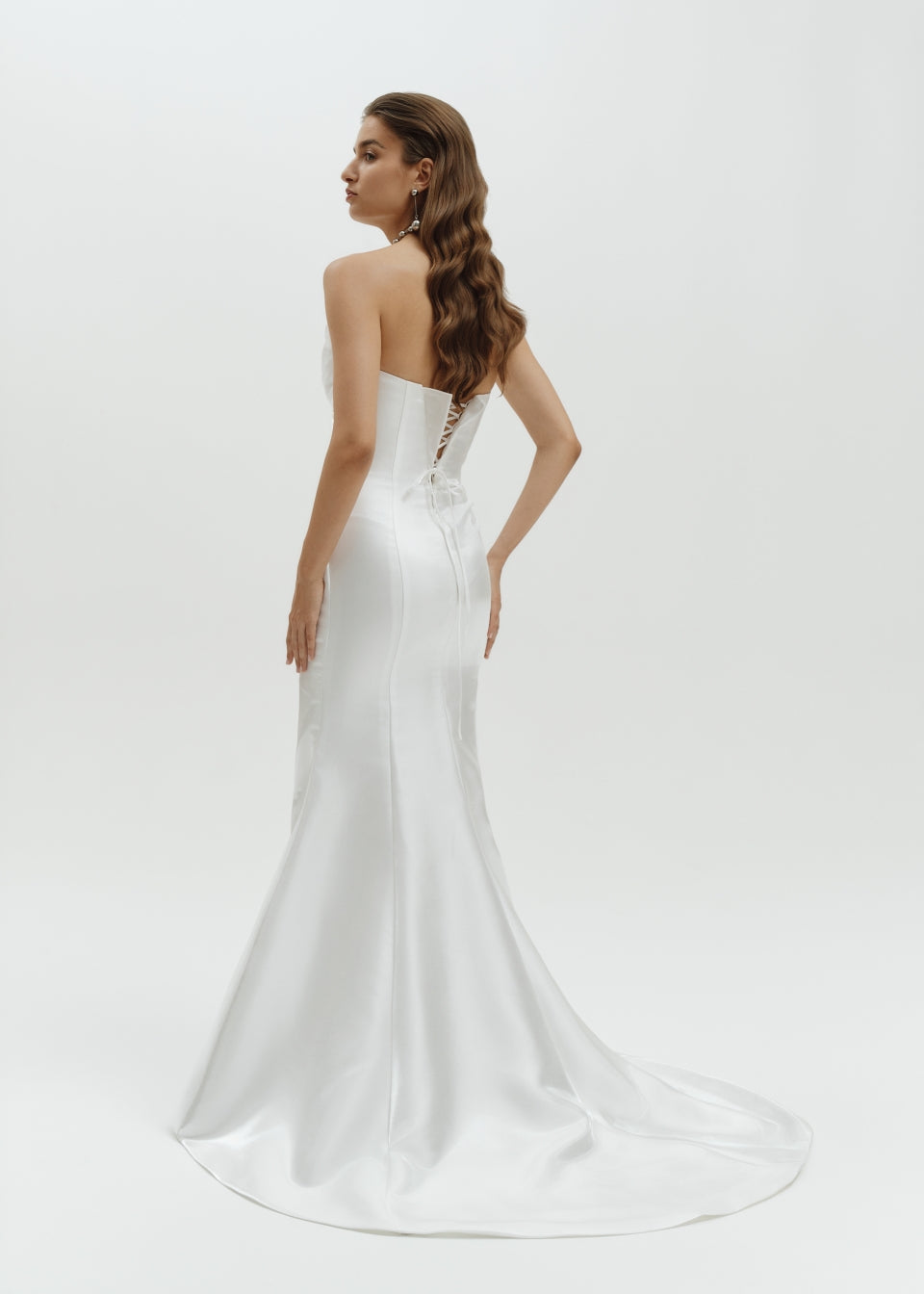 Woman wearing a strapless liquid organza fitted wedding dress on a white background