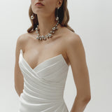 Woman wearing a strapless liquid organza fitted wedding dress and pearl necklace on a plain background