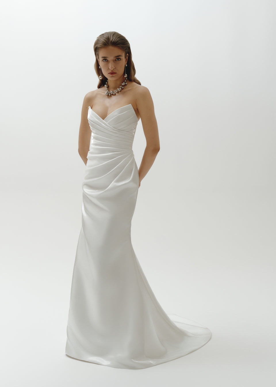 Woman wearing a strapless liquid organza fitted wedding dress on a plain background