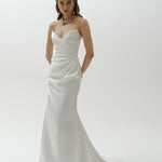 Woman wearing a strapless liquid organza fitted wedding dress on a plain background