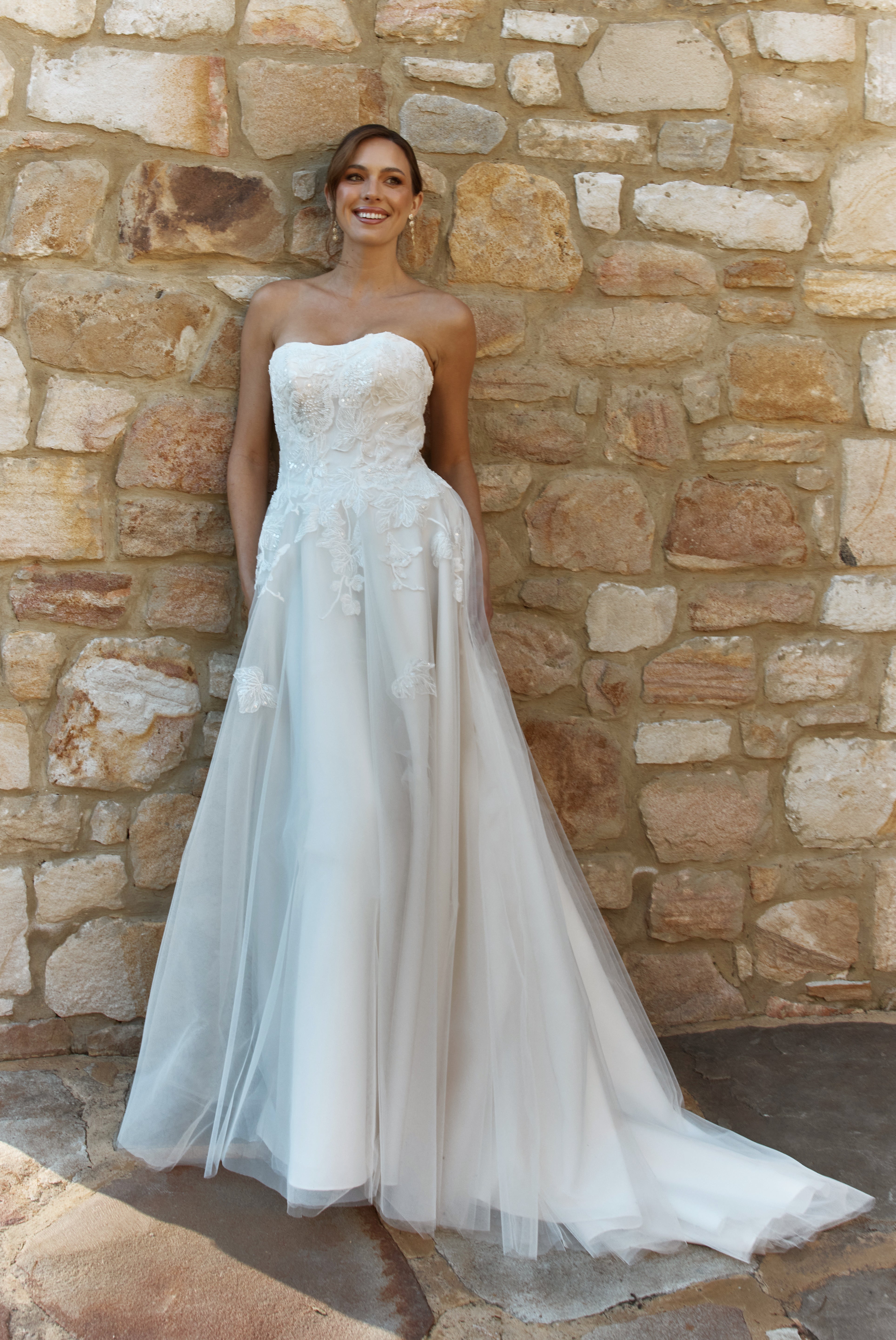 Woman in a Lace A-Line Wedding Dress standing against a stone wall.