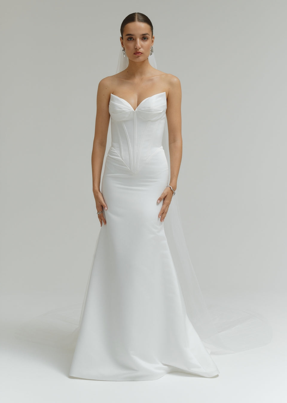 Woman wearing a strapless white wedding dress on a plain background