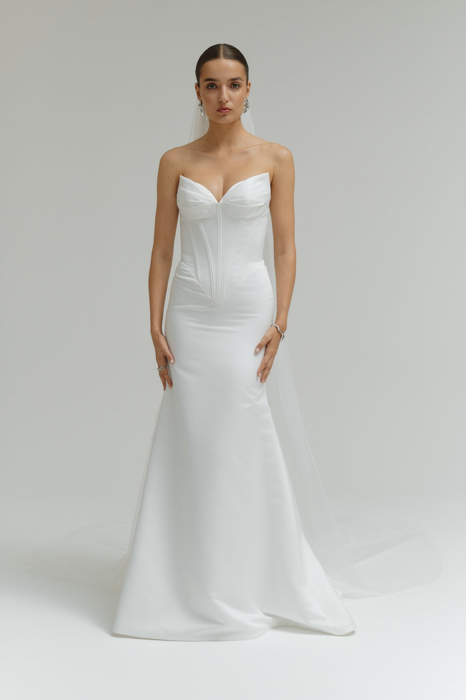 Woman wearing a strapless white wedding dress on a plain background