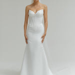 Woman wearing a strapless white wedding dress on a plain background