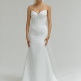 Woman wearing a strapless white wedding dress on a plain background