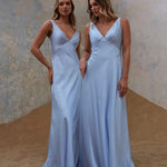 Two women in light blue bridesmaid gowns standing in a modern indoor setting.