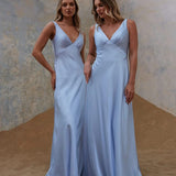 Two women in light blue bridesmaid gowns standing in a modern indoor setting.