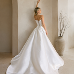 Woman in a Modern Mikado Wedding Dress standing in a modern indoor setting with concrete walls and natural light.