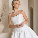 Woman in a Modern Mikado Wedding Dress with a pearl necklace against a warm-toned wall.