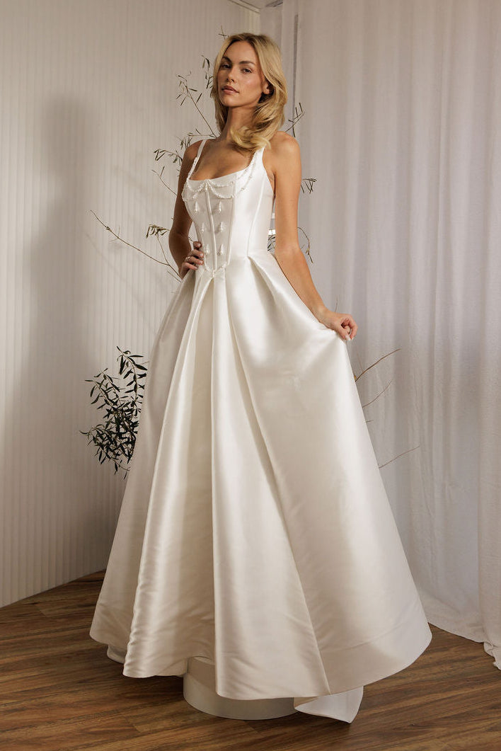 Woman in a Mikado ballgown wedding dress standing in a room with white curtains.