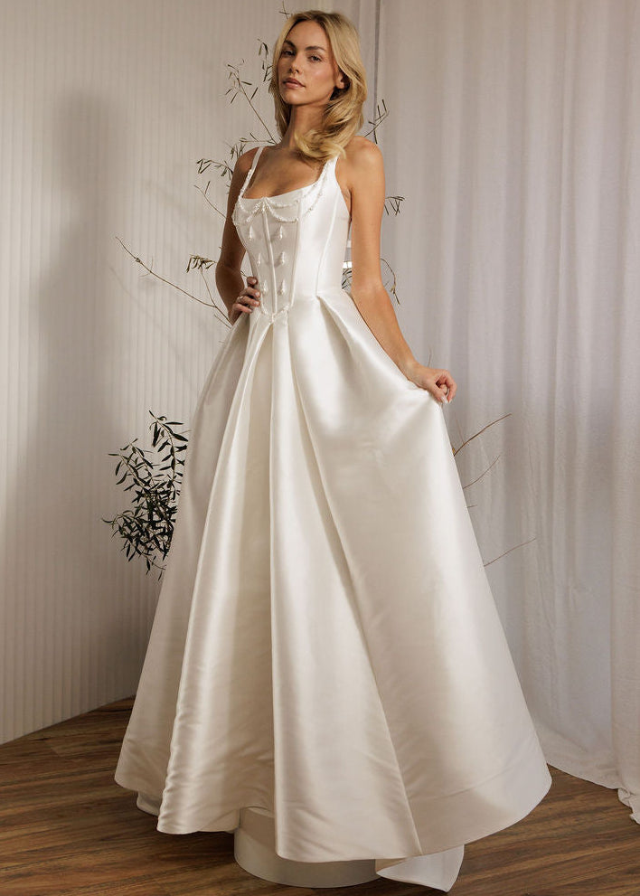 Woman in a Mikado ballgown wedding dress standing in a room with white curtains.
