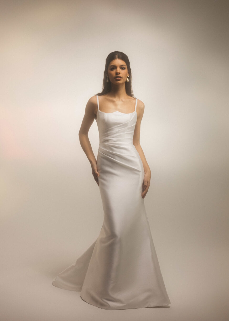 Bride wearing the Bellevue modern fitted wedding dress with thin straps and draped bodice, photographed against a soft studio background.