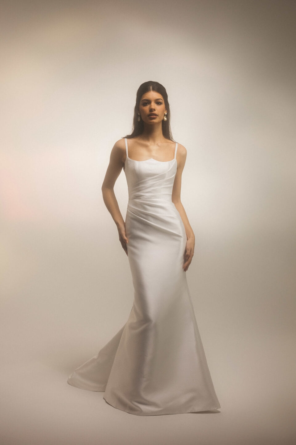 Bride wearing the Bellevue modern fitted wedding dress with thin straps and draped bodice, photographed against a soft studio background.