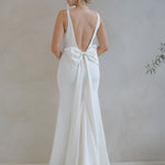 Woman wearing a Crepe Fit and Flare Wedding Dress with a bow detail in a minimalistic setting.